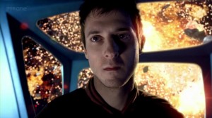 Rory stares at the camera, unmoved, with exploding Cyberman ships behind him