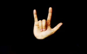 A light-skinned hand with fingers spread except the middle and ring finger which are folded into the palm.  Sign language for I love you.
