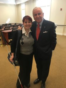 Colleen stands next to the president of Highpoint U, Dr. Nido Qubein both in suit jackets in the lecture hall of the business school